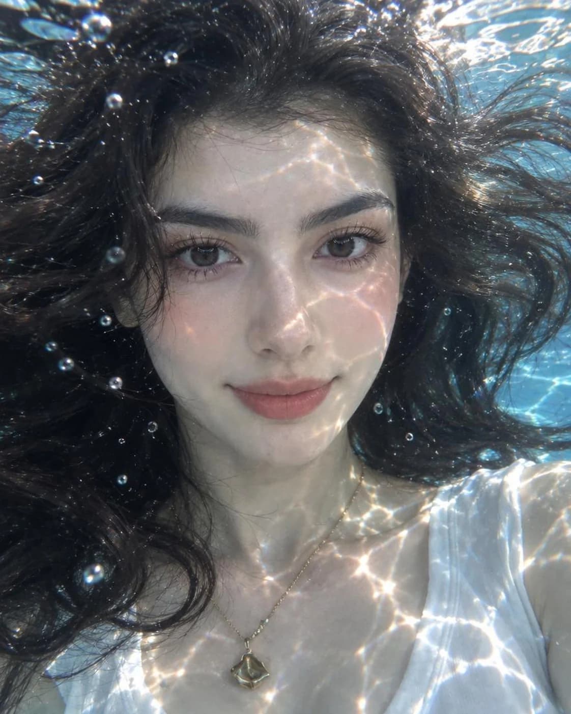 Close-up portrait of a woman in a pool with caustic light patterns on her skin