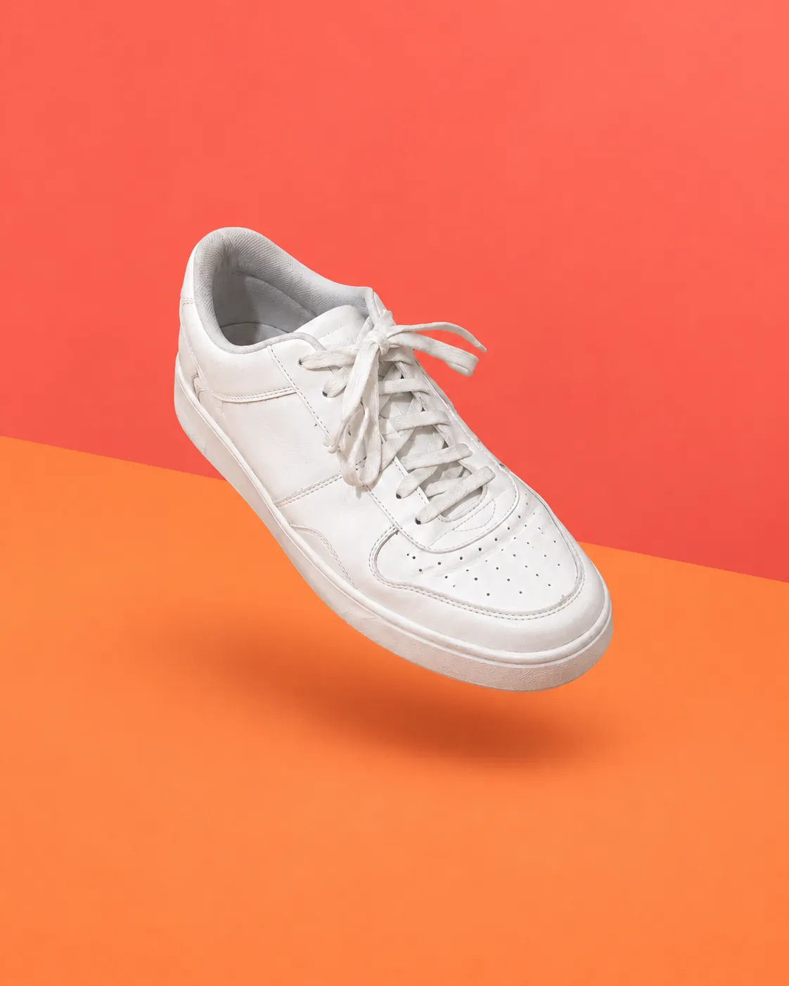 White sneaker floating over a coral and tangerine color-block backdrop